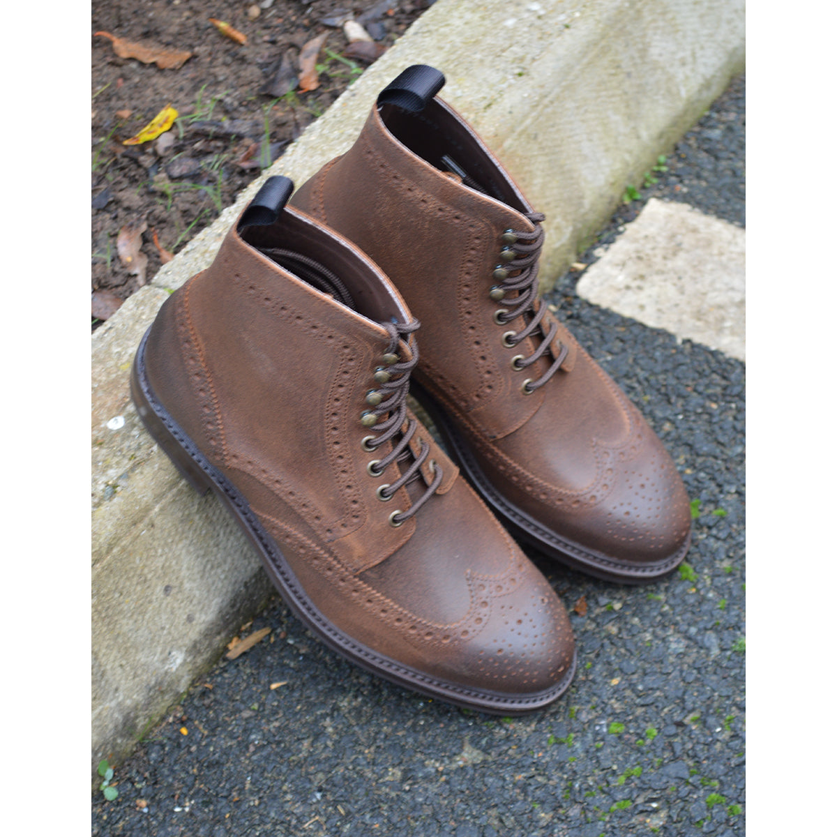 A dark brown lace-up brogue boot with a rubber sole and visible stitching on the upper part.