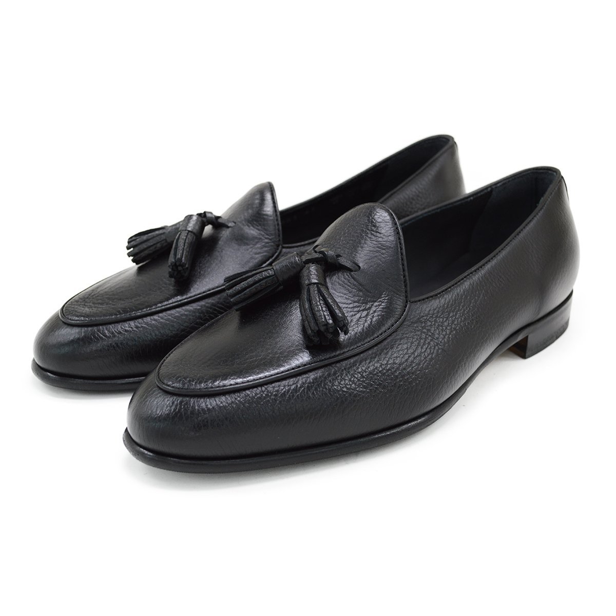 A black deerskin leather tassel Belgian loafer with an almond-shaped toe and a subtle tread sole, displayed against a white background.