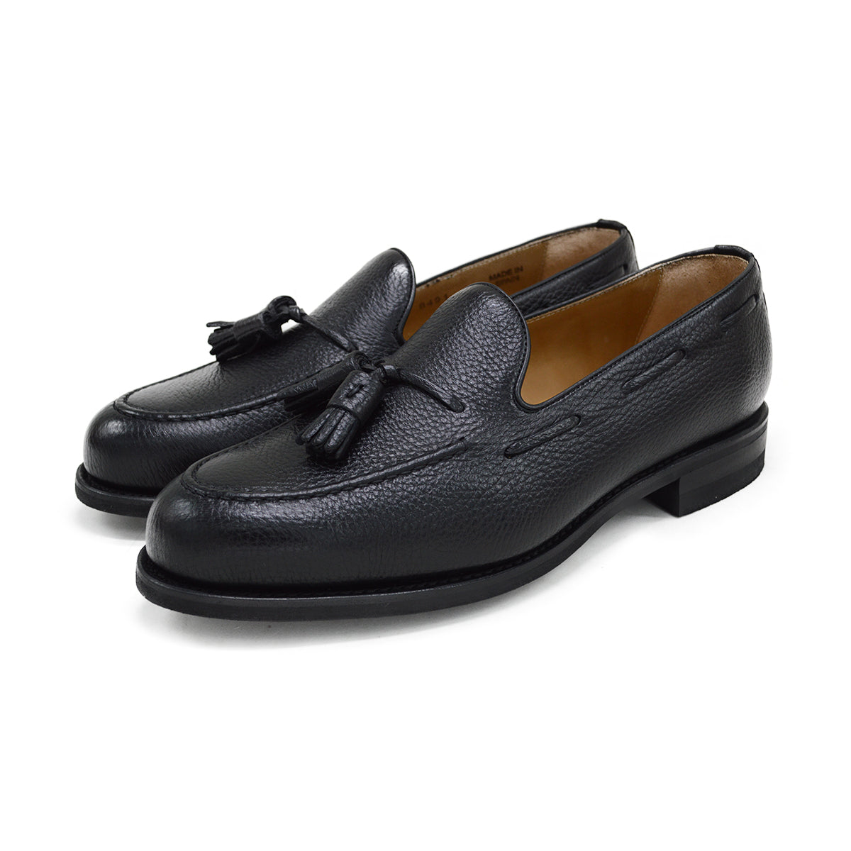 A black deerskin slip-on loafer with a tassel detail on the vamp, featuring a classic round toe and a low heel.