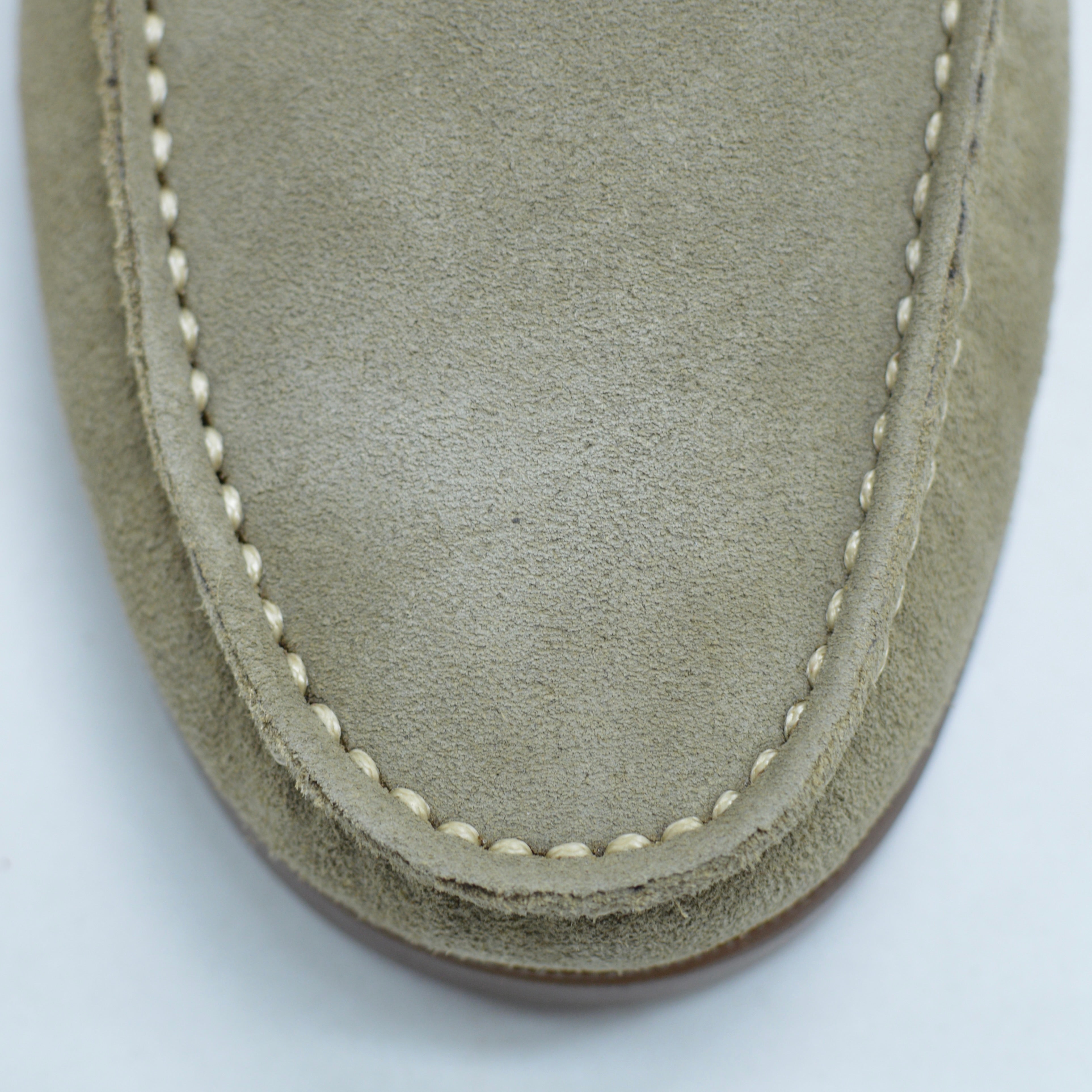 Close-up of a sand suede shoe with white stitching on a light gray background