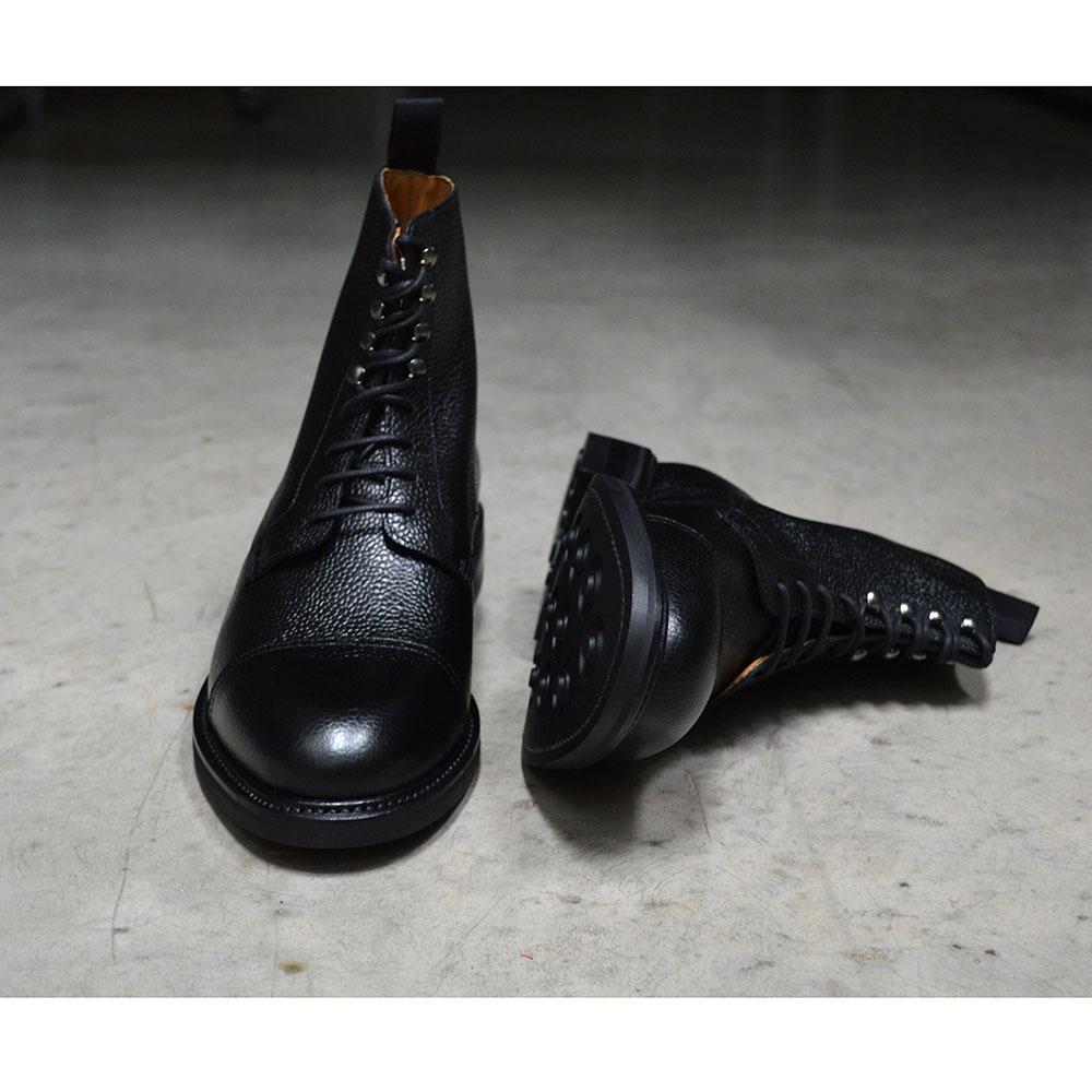 A Berwick 1707 black grain toe cap boot with a full lace-up construction and a round toe shape, set against a polished concrete background.