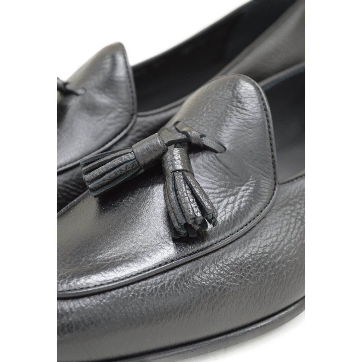 A black deerskin leather tassel Belgian loafer with an almond-shaped toe and a subtle tread sole, displayed against a white background.
