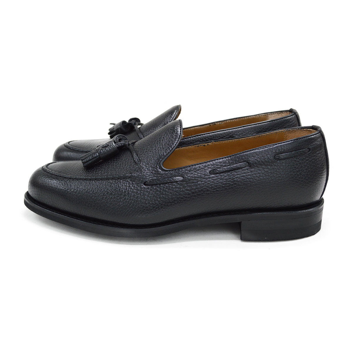A black deerskin slip-on loafer with a tassel detail on the vamp, featuring a classic round toe and a low heel.