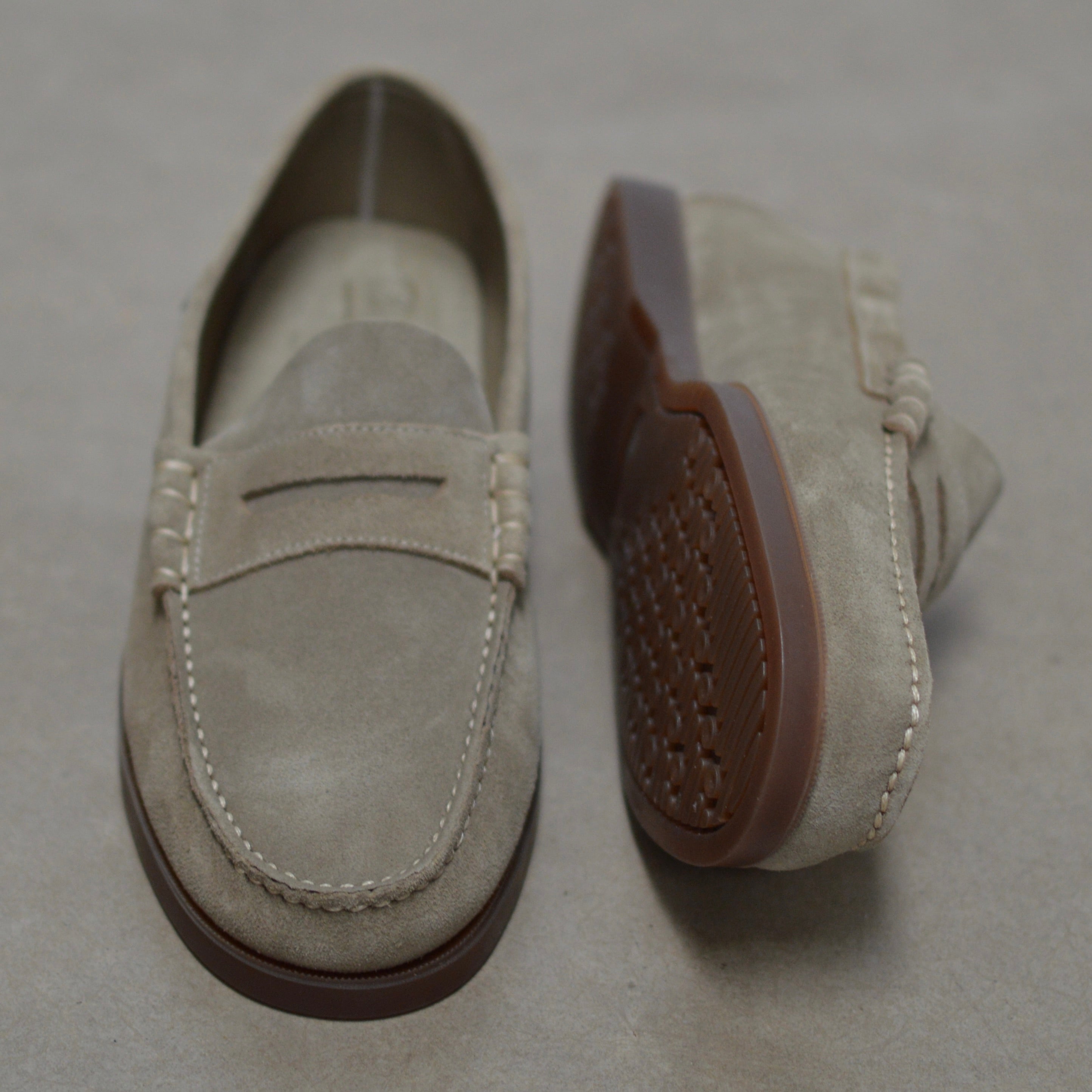 Pair of sand loafers with brown soles on a gray background