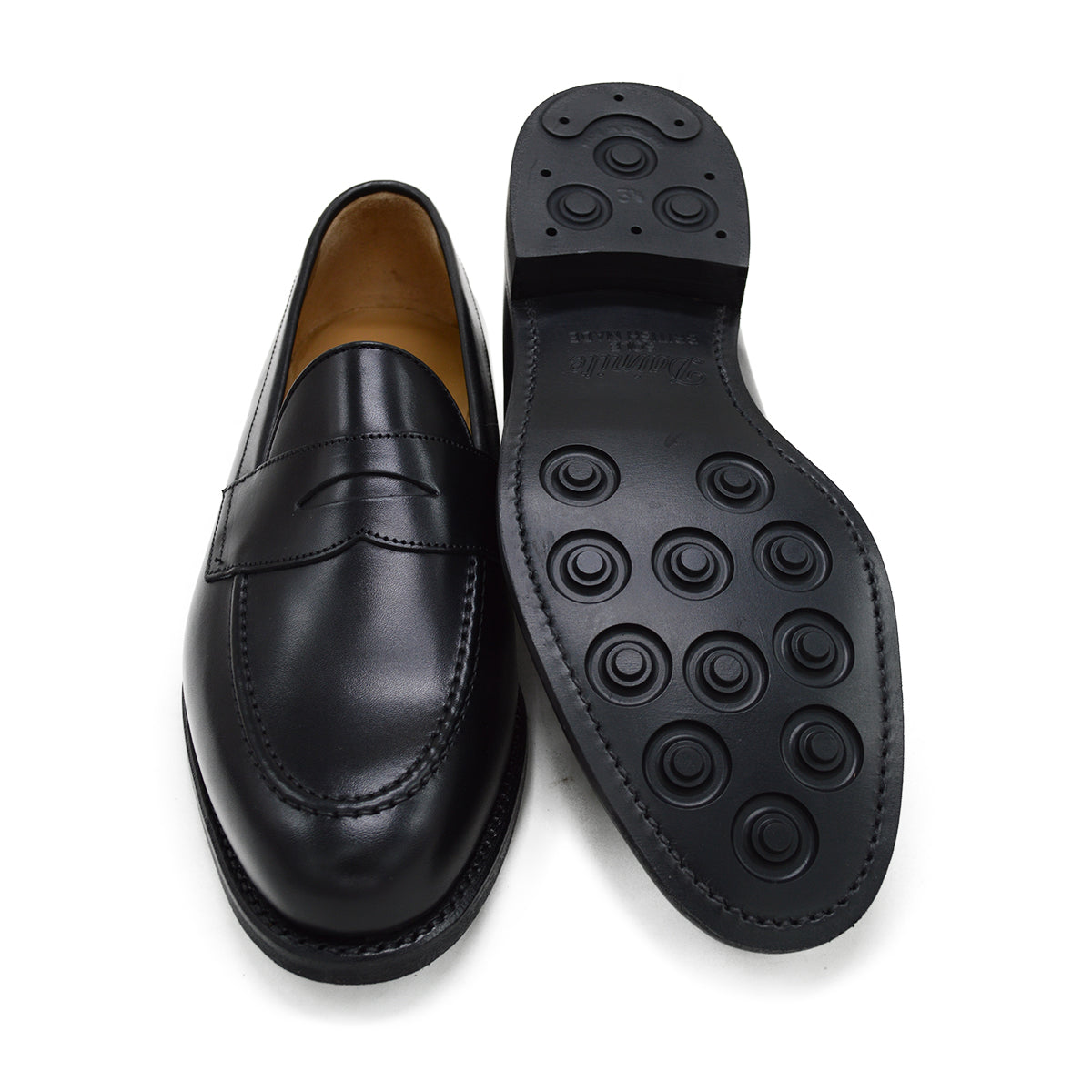 A black calf leather penny loafer with a Dainite rubber sole, showing a classic round toe shape and the iconic penny slot detail.