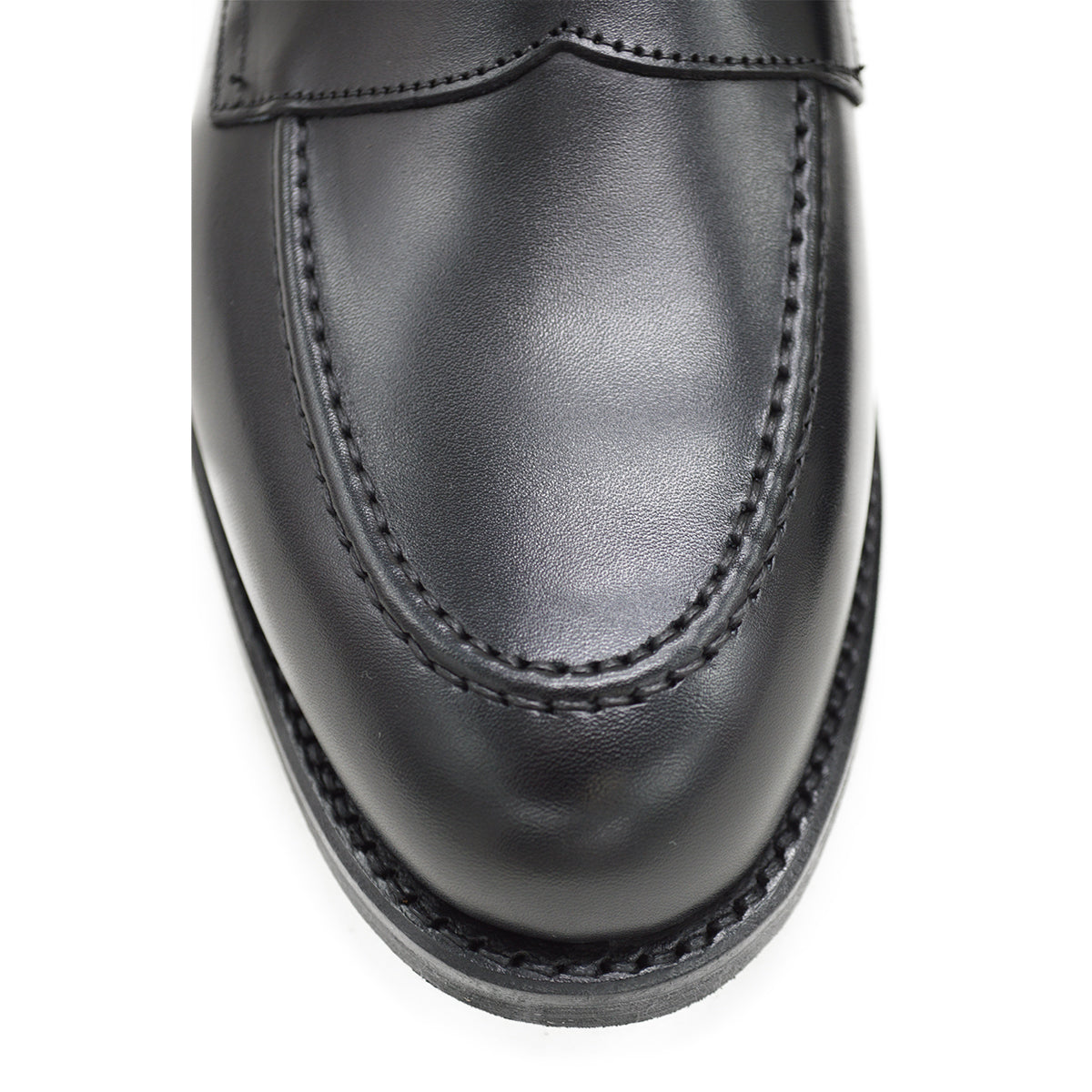 A black calf leather penny loafer with a Dainite rubber sole, showing a classic round toe shape and the iconic penny slot detail.