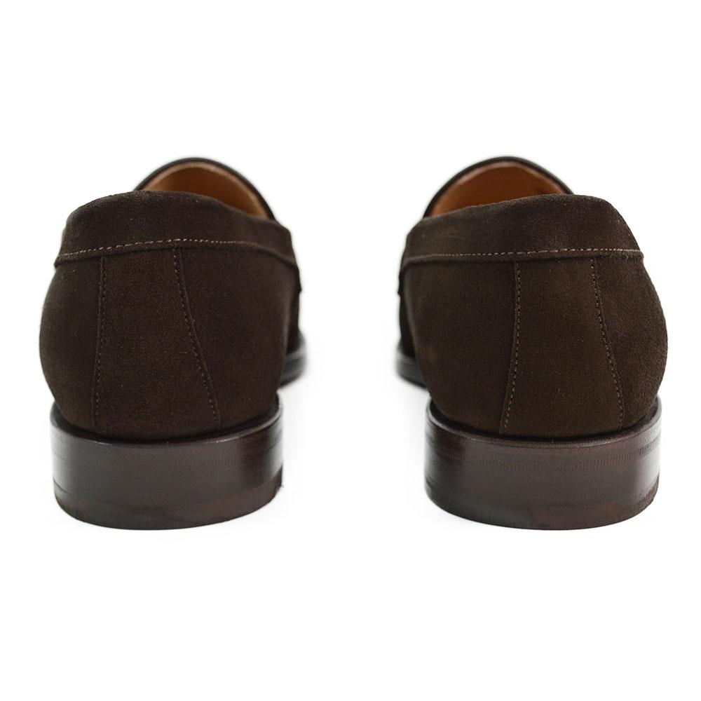 A dark brown suede penny loafer with a round toe shape and a studded Dainite sole.