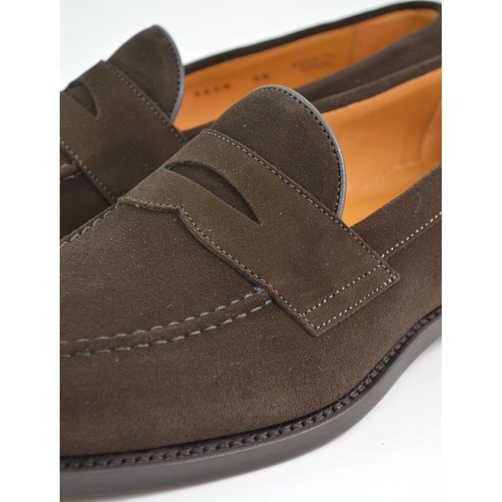 A dark brown suede penny loafer with a round toe shape and a studded Dainite sole.