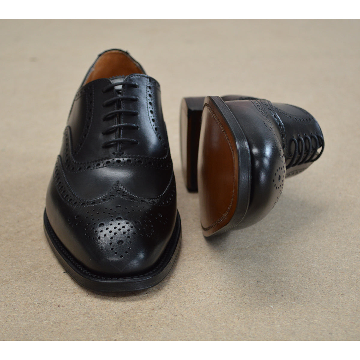 A Berwick 1707 black Oxford brogue shoe with brogue detailing and a lace-up closure. The shoe is made of smooth leather and appears to be sturdy and durable.