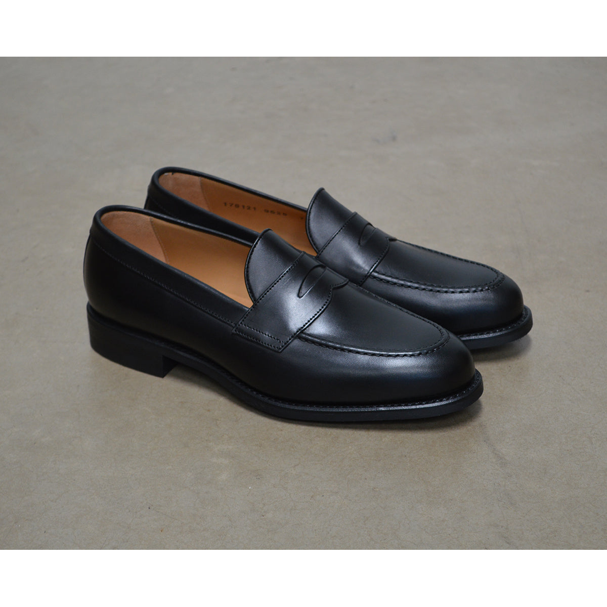 A black calf leather penny loafer with a Dainite rubber sole, showing a classic round toe shape and the iconic penny slot detail.