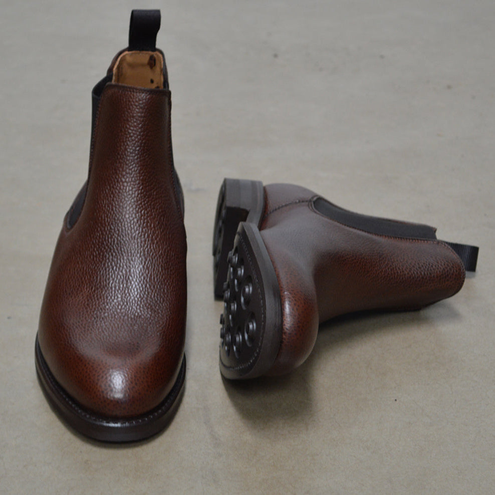 A dark brown grain leather Chelsea boot with a black elastic side panel and a round toe. The boot has a low heel and a goodyear welted dainite rubber sole.