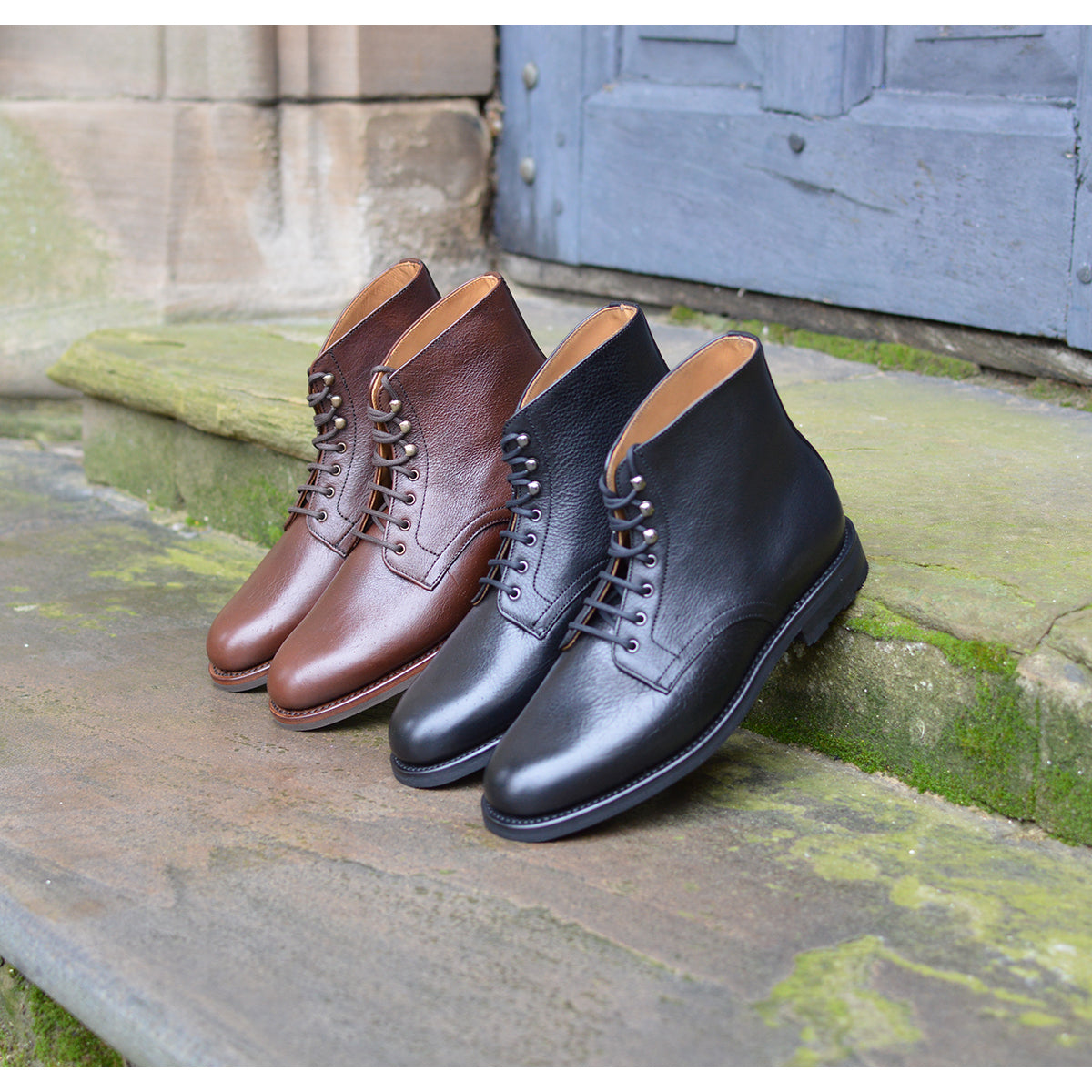 Pair of brown and black leather boots on a stone step with a wooden door in the background.