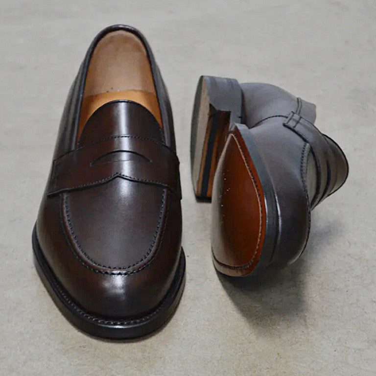 A dark brown Berwick 1707 Penny Loafer with a closed toe and loafers style heel, displayed on a polished concrete background.