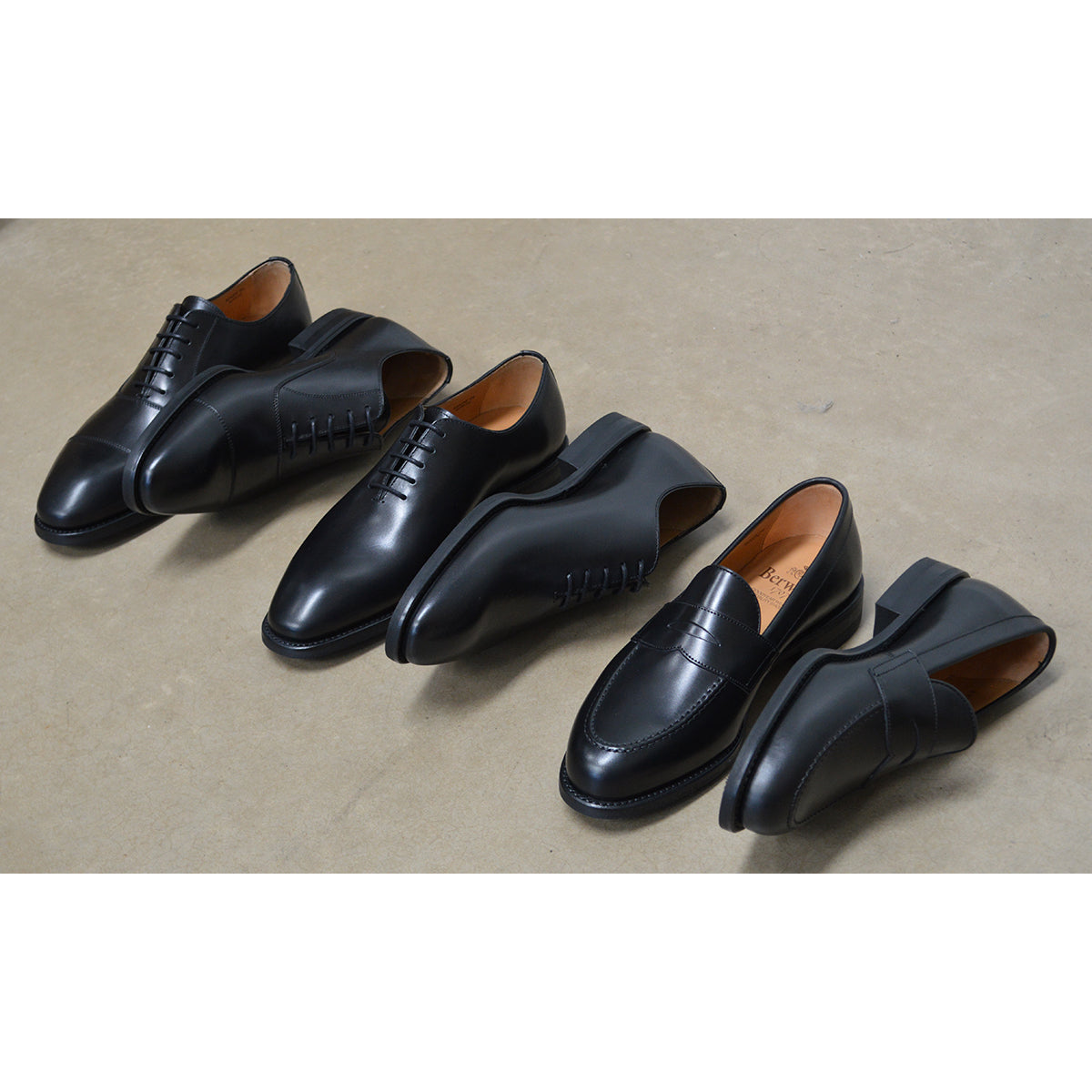 A Berwick 1707 black leather Oxford shoe with a chisel toe and lace-up closure with a Dainite rubber studded sole, on a polished concrete background.