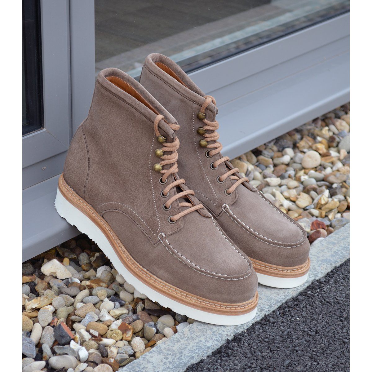 A grey and tan suede apron boot with lace-up closure, featuring a white sole and a natural welt.