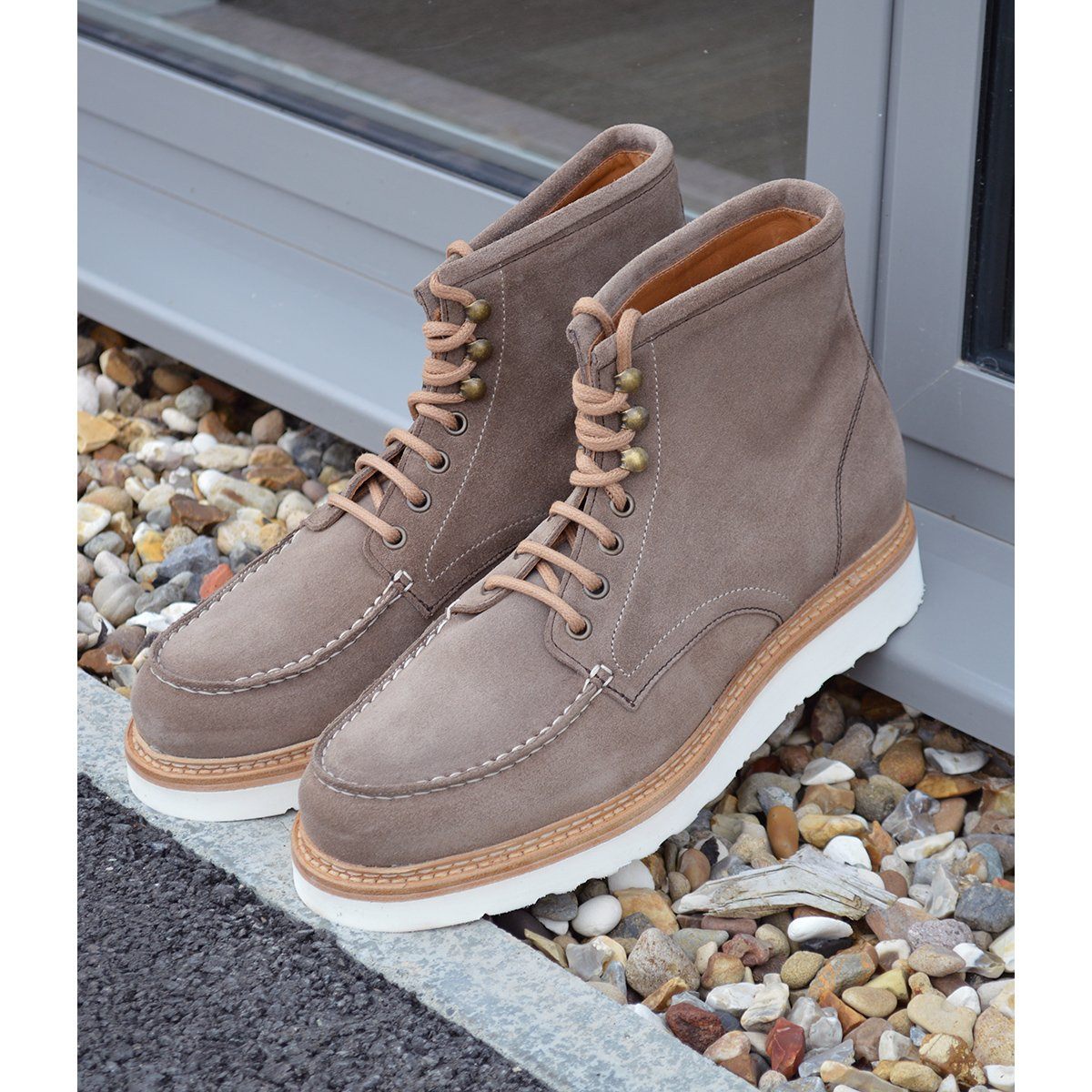 A grey and tan suede apron boot with lace-up closure, featuring a white sole and a natural welt.