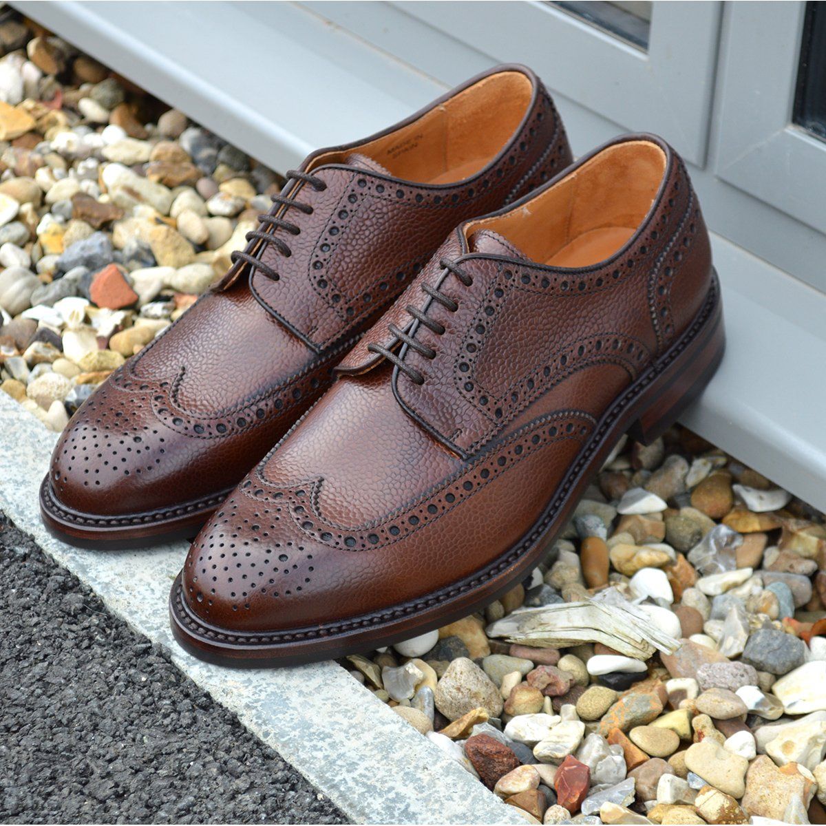 A Berwick 1707 brown brogue derby shoe with a round toe shape and lace-up closure. It features a grainy texture and brogue detailing & Dainite soles