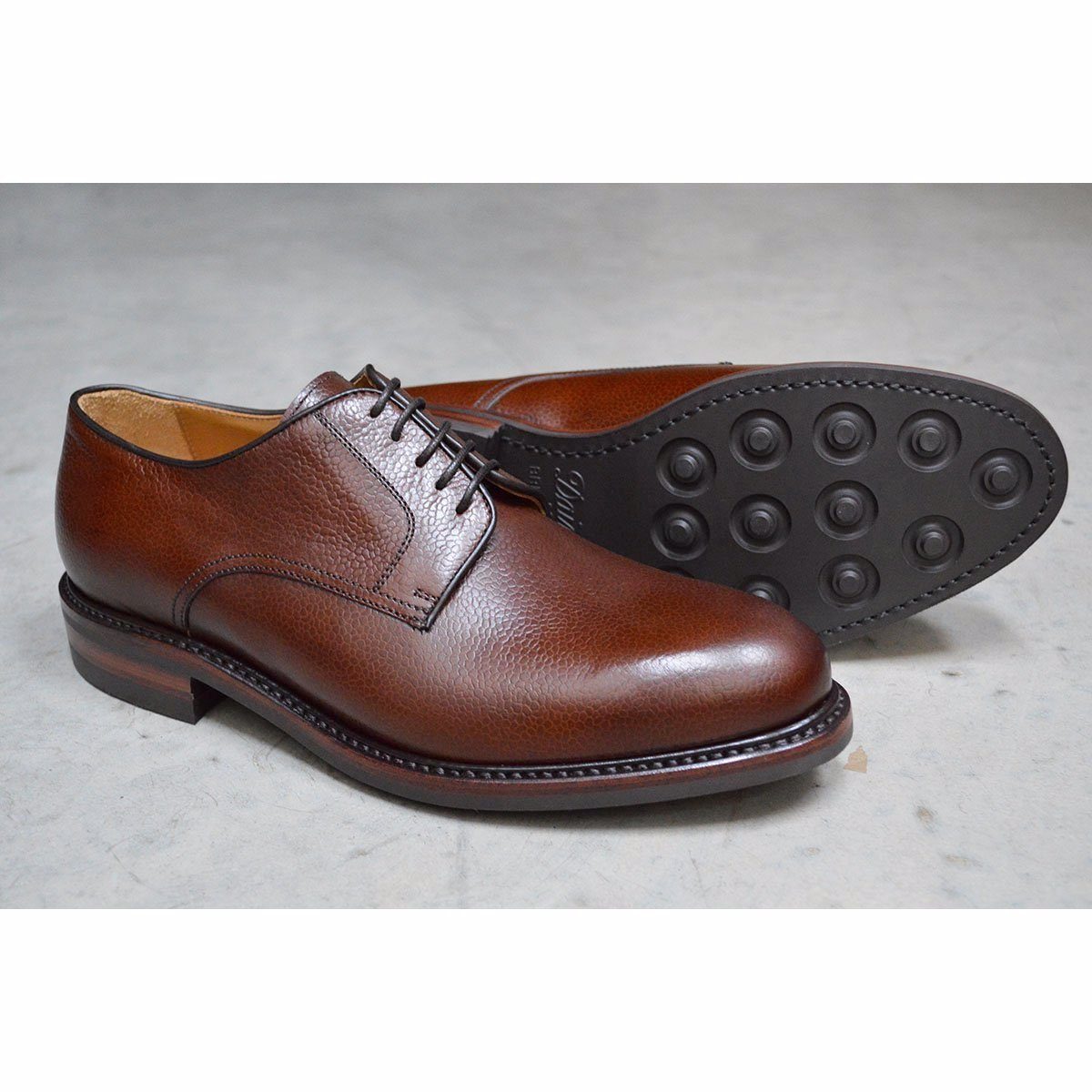 A dark brown, grainy-textured leather derby shoe with a round toe and classic lace-up closure & Dainite soles
