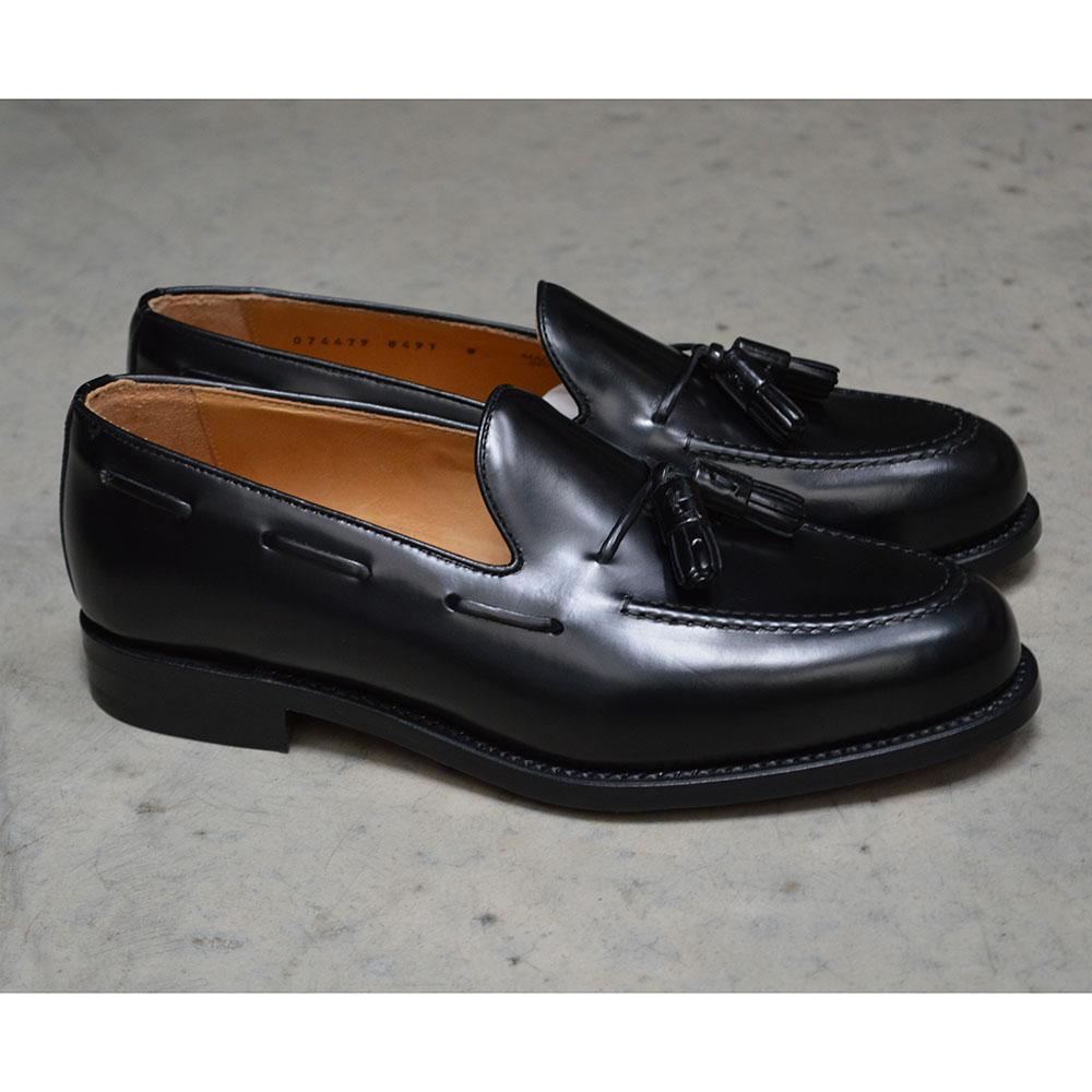 A black tasselled slip-on shoe with a high shine finish and a classic round toe.