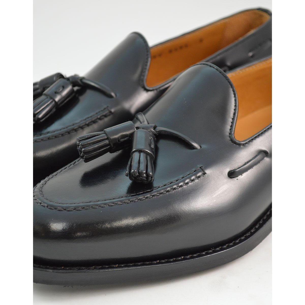 A black tasselled slip-on shoe with a polished, smooth upper and a classic round toe. The shoe is set against a white background.