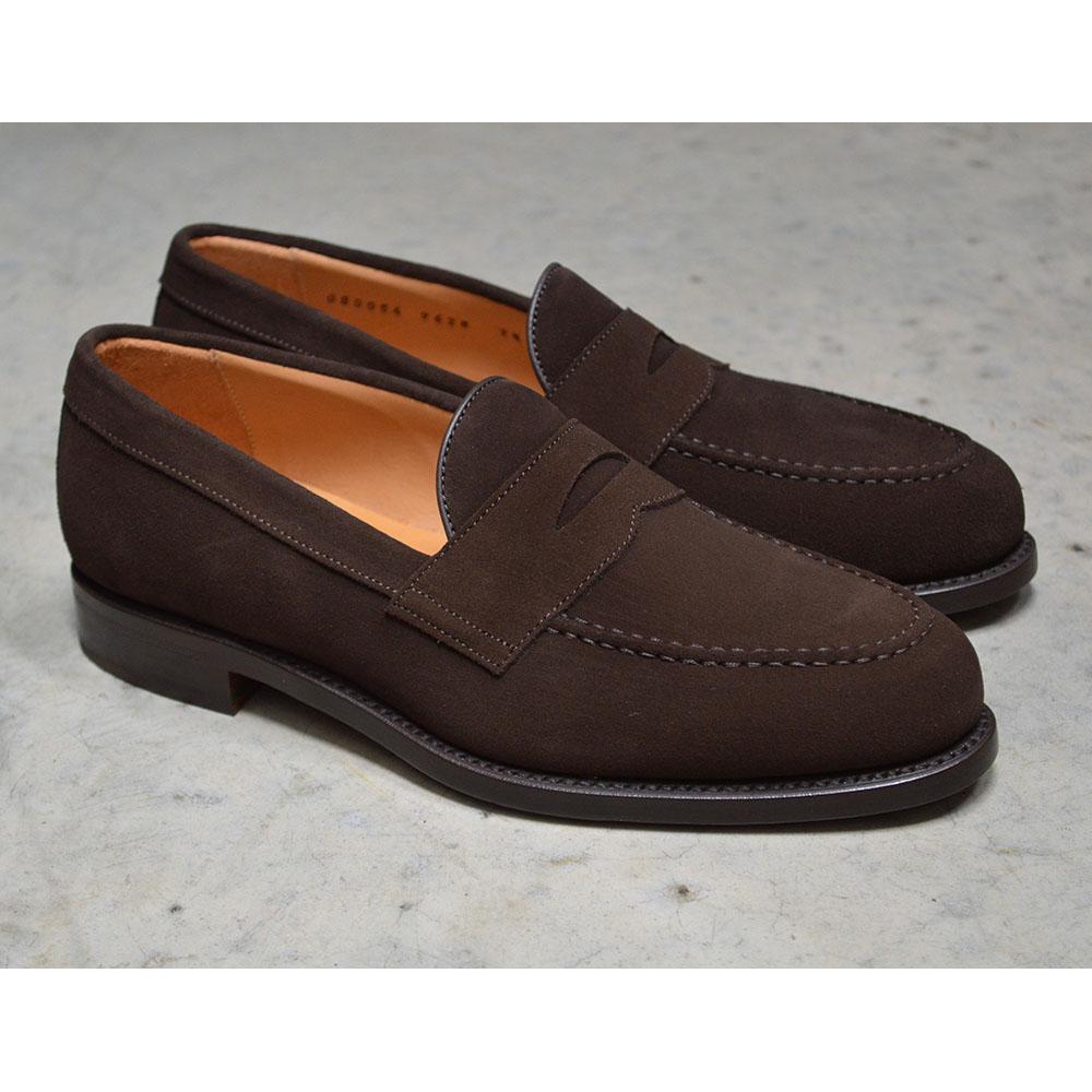 A dark brown suede penny loafer with a Goodyear welted leather sole, displayed on a polished concrete background.
