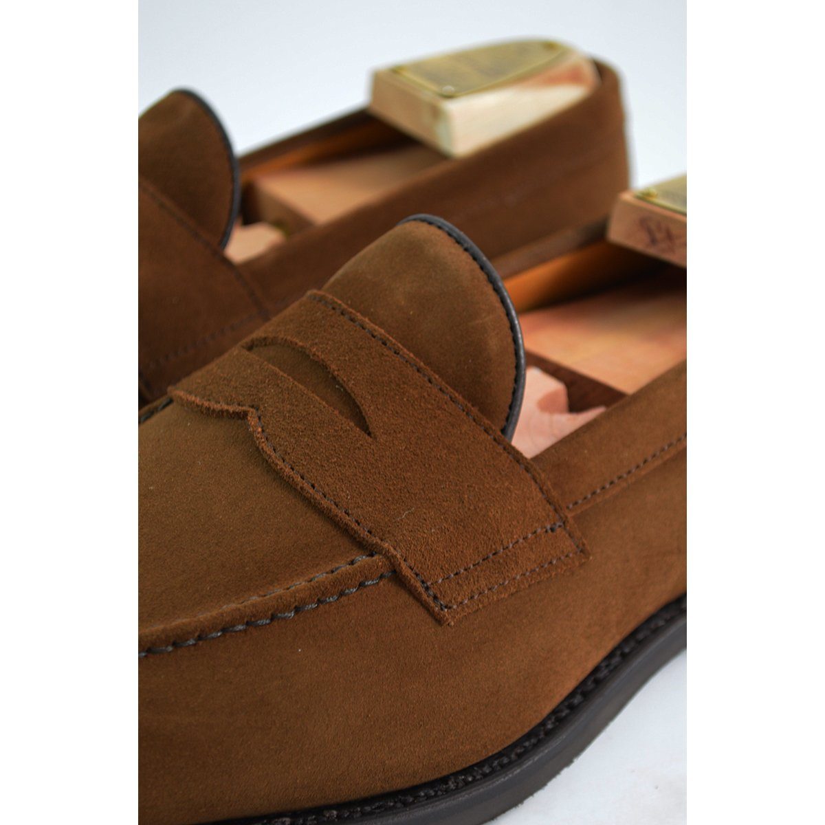 A brown suede penny loafer with a Dainite rubber sole, showing a classic round toe shape and a signature penny slot detail & Dainite Soles