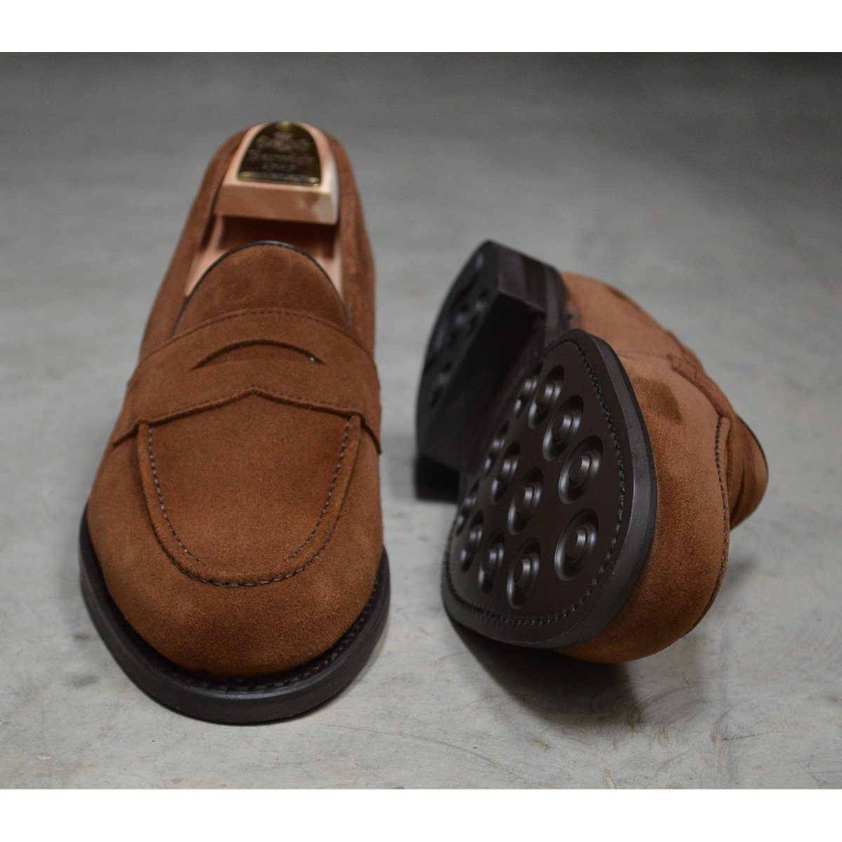 A brown suede penny loafer with a Dainite rubber sole, showing a classic round toe shape and a signature penny slot detail & Dainite Soles