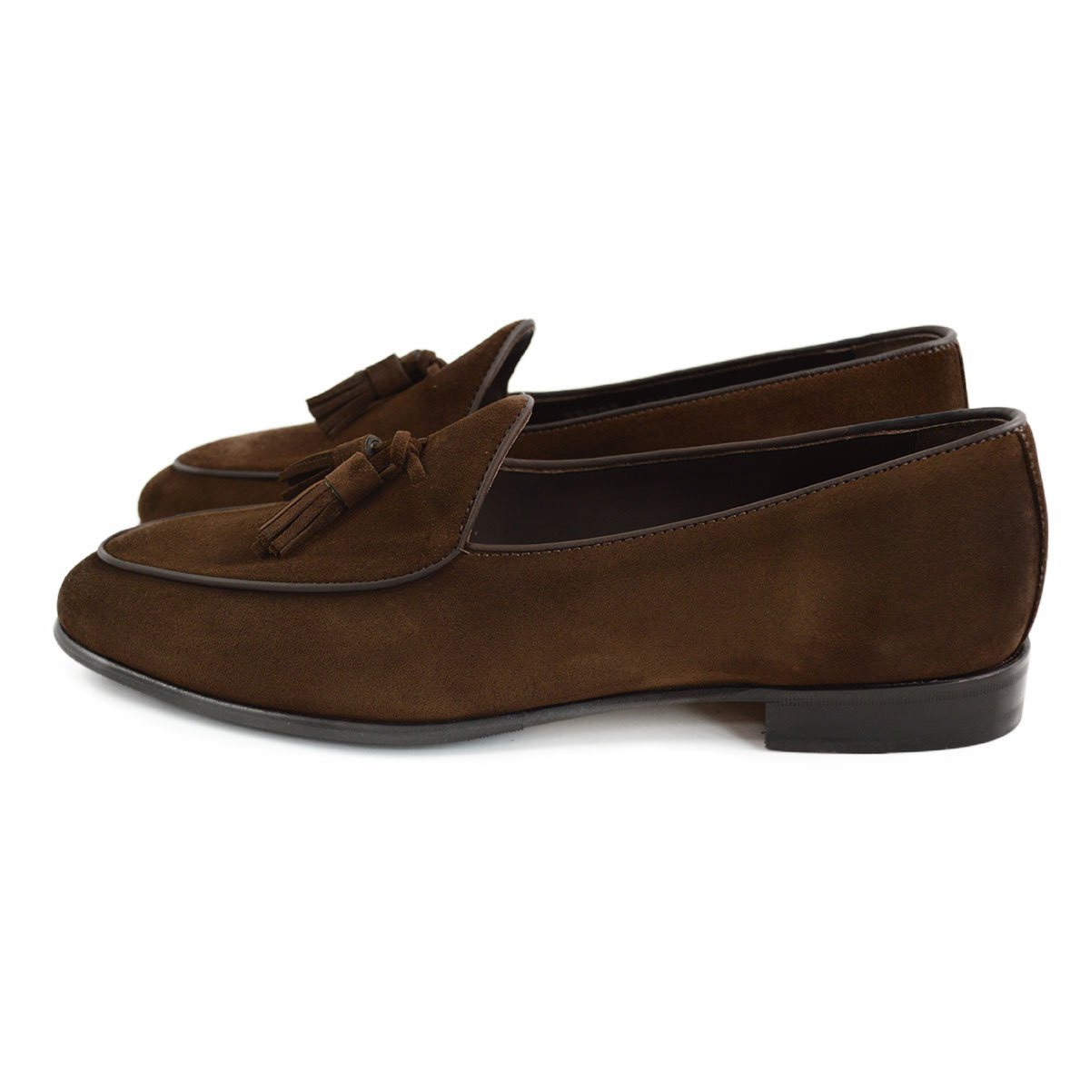 A dark brown suede tassel loafer with a Vegano Moka leather trim, displaying an almond-shaped toe and a fine ridged rubber sole.