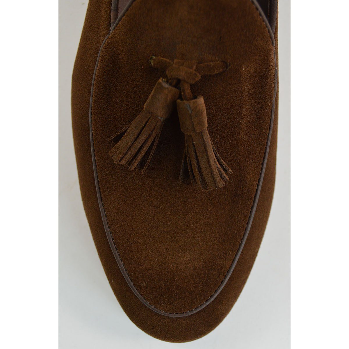 A dark brown suede tassel loafer with a Vegano Moka leather trim, displaying an almond-shaped toe and a fine ridged rubber sole.