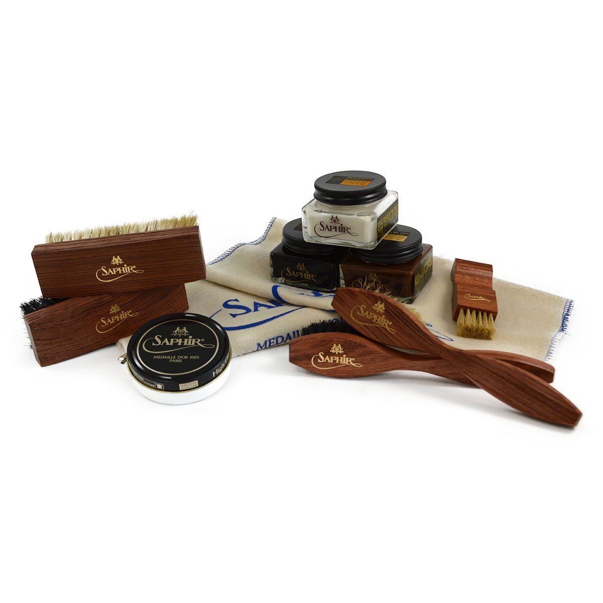An assortment of shoe care products from Saphir Medaille D'Or including polishing cloths, brushes, cream polishes in black and medium brown, a shoe bag and a neutral wax polish.