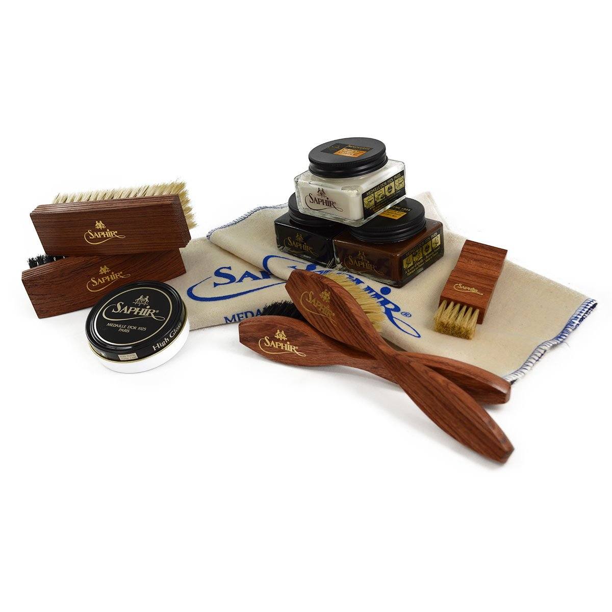 An assortment of shoe care products from Saphir Medaille D'Or including polishing cloths, brushes, cream polishes in black and medium brown, a shoe bag and a neutral wax polish.