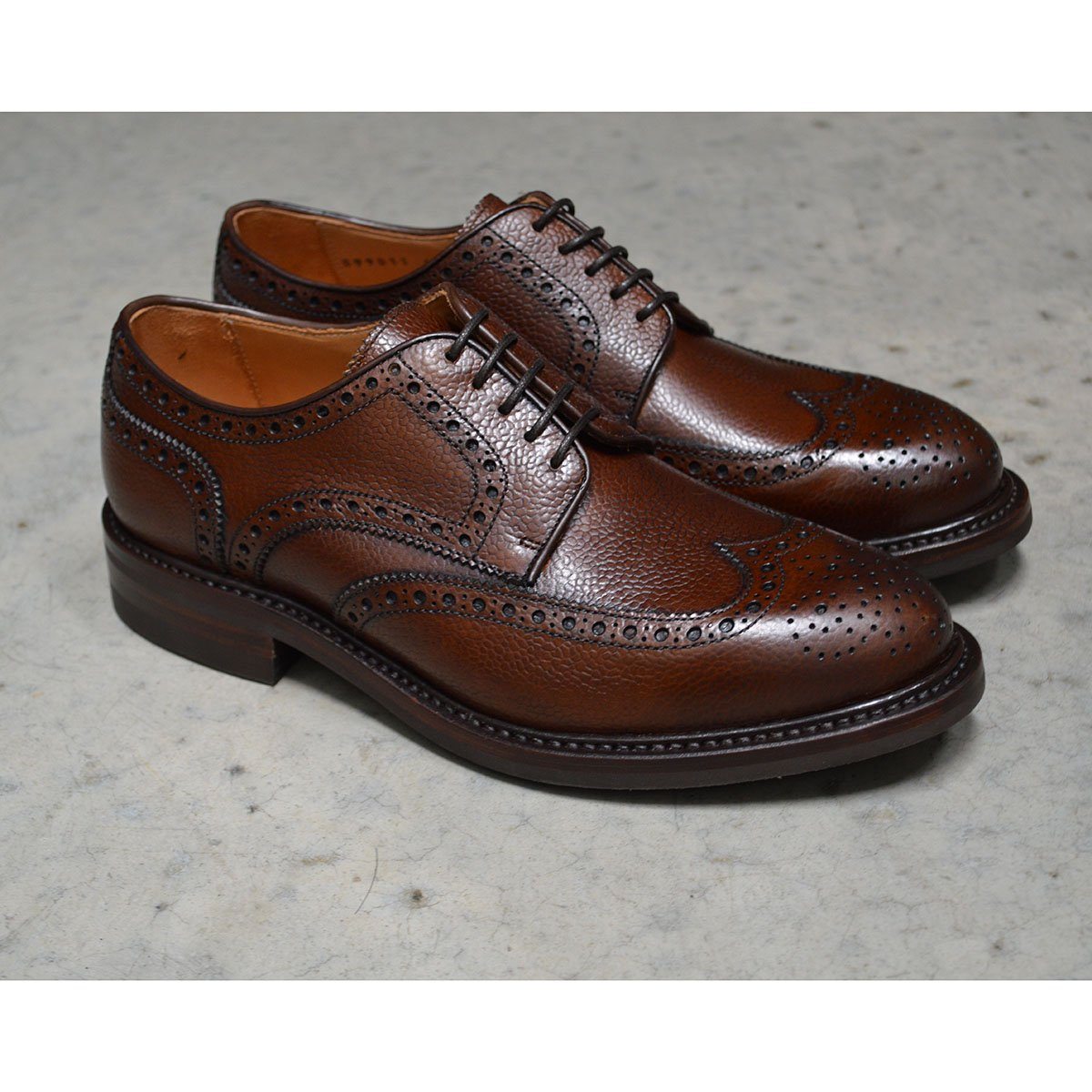A Berwick 1707 brown brogue derby shoe with a round toe shape and lace-up closure. It features a grainy texture and brogue detailing & Dainite soles