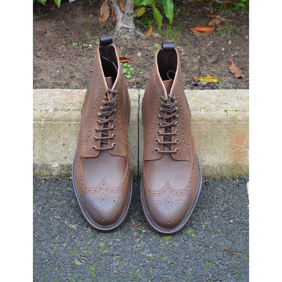 A dark brown lace-up brogue boot with a rubber sole and visible stitching on the upper part.
