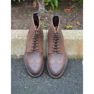 A dark brown lace-up brogue boot with a rubber sole and visible stitching on the upper part.