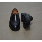 A black calf leather penny loafer with a Dainite rubber sole, showing a classic round toe shape and the iconic penny slot detail.