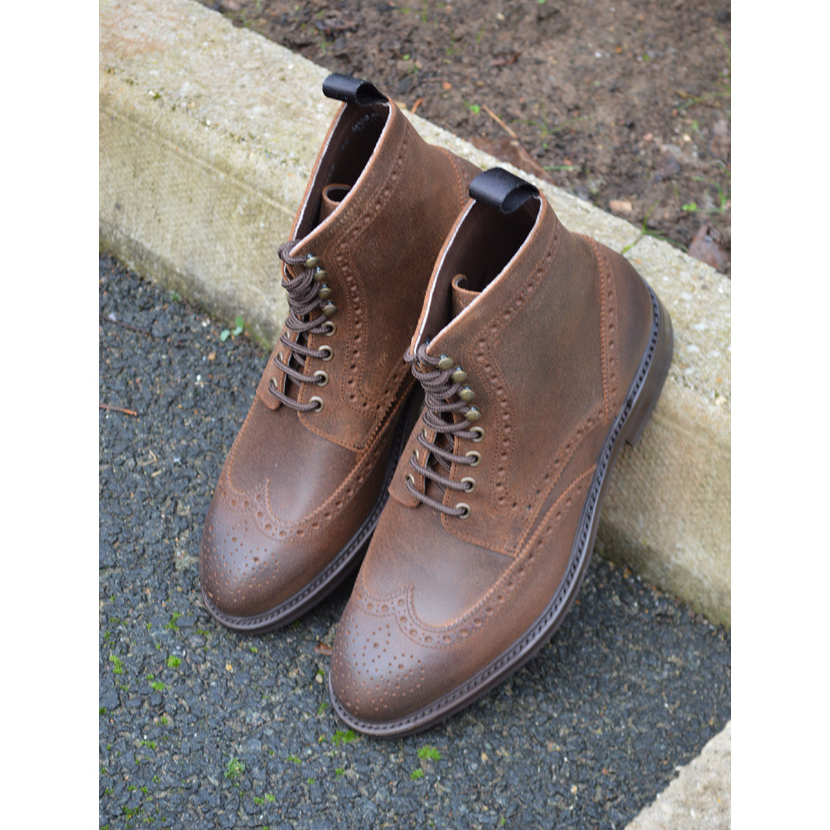 A dark brown lace-up brogue boot with a rubber sole and visible stitching on the upper part.