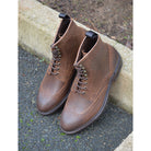 A dark brown lace-up brogue boot with a rubber sole and visible stitching on the upper part.