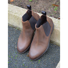 A dark brown Chelsea boot with a waxy leather finish and a contrasting black elastic side panel. The boot has a low heel and a small pull tab at the rear.