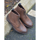 A dark brown lace-up brogue boot with a rubber sole and visible stitching on the upper part.