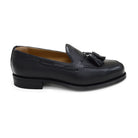 A black deerskin slip-on loafer with a tassel detail on the vamp, featuring a classic round toe and a low heel.