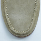 Close-up of a sand suede shoe with white stitching on a light gray background