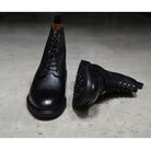 A Berwick 1707 black grain toe cap boot with a full lace-up construction and a round toe shape, set against a polished concrete background.