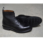 A Berwick 1707 black grain toe cap boot with a full lace-up construction and a round toe shape, set against a polished concrete background.