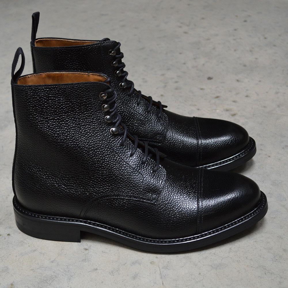 A Berwick 1707 black grain toe cap boot with a full lace-up construction and a round toe shape, set against a polished concrete background.