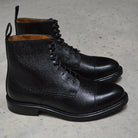 A Berwick 1707 black grain toe cap boot with a full lace-up construction and a round toe shape, set against a polished concrete background.