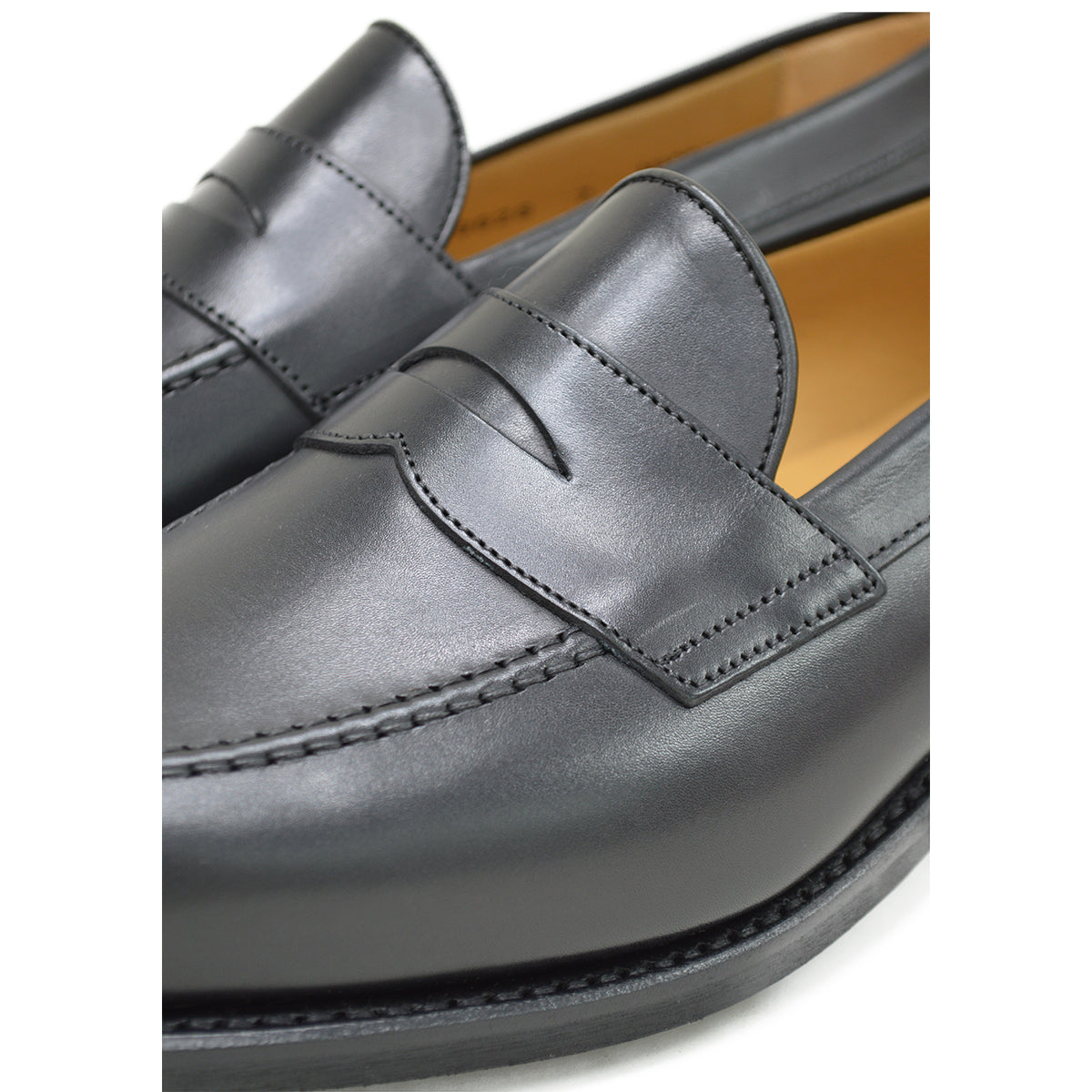 A black calf leather penny loafer with a Dainite rubber sole, showing a classic round toe shape and the iconic penny slot detail.