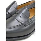 A black calf leather penny loafer with a Dainite rubber sole, showing a classic round toe shape and the iconic penny slot detail.