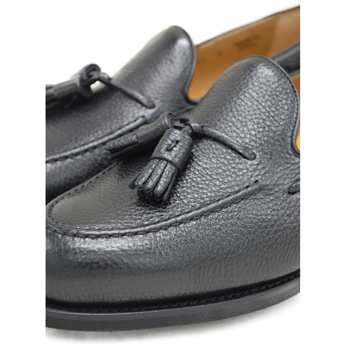 A black deerskin slip-on loafer with a tassel detail on the vamp, featuring a classic round toe and a low heel.