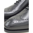 A black wholecut Oxford brogue shoe with a brogue pattern on the upper, a lace-up closure, and a goodyear welted leather sole.