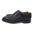 A Berwick 1707 black Oxford brogue shoe with brogue detailing and a lace-up closure. The shoe is made of smooth leather and appears to be sturdy and durable.
